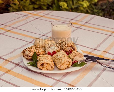 Tasty pancakes with home made cheese on white plate closeup. Crepes stuffed with cheese, and glass of milk on checked table cloth.