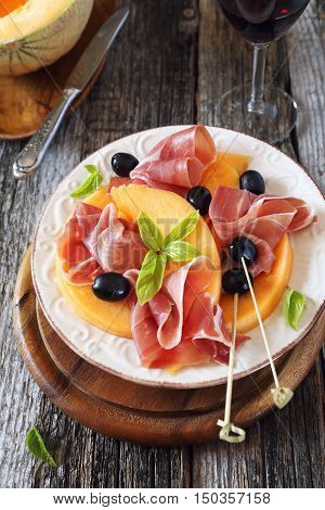 Prosciutto with melon and glass of red wine.Traditional Italian appetizer