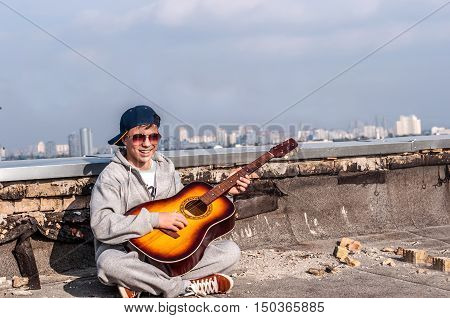 Young man playing on guitar on the roof of a tall building