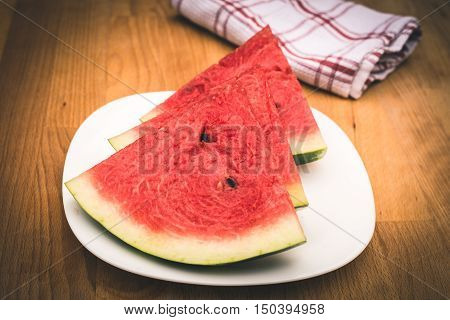 Watermelon slices on the white porcelain plate served with napkin straw-coloured wooden background