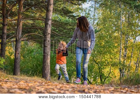Mother and son running on path in autumn forest. Family at nature autumn bright sunny day fallen yellow leaves underfoot.