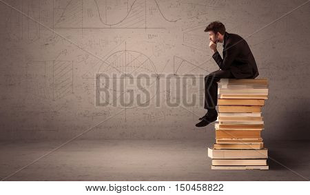 A serious businessman in suit sitting on a pile of giant books in front of a greyish brown wall with drawn lines, angles, numbers, circles and curves.