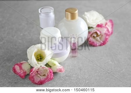 Cosmetic bottles and eustoma flowers on light wooden background