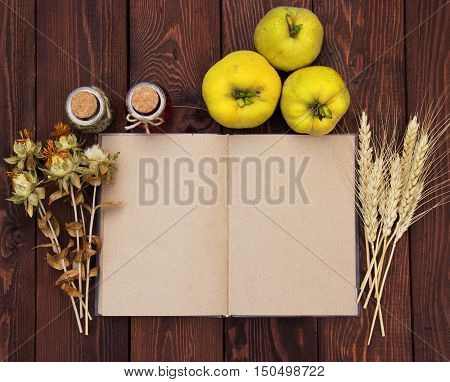 Kitchen book with blank pages to write text on the wooden background with quince and wheat spikelets. Copy space. Food background. Autumn harvest. Open notebook with blank pages on wooden background.