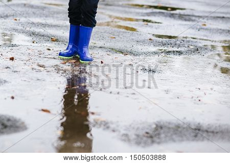 Boy In Rubber Blue Rainboots Jumping To Dirty Puddle
