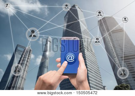 Hand holding smartphone and click on button with at sign linked with people icons. Email marketing newsletter and bulk mail concepts.