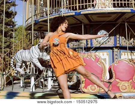 cool real modern teenage girl with candy near carousels at amusement park walking, having fun