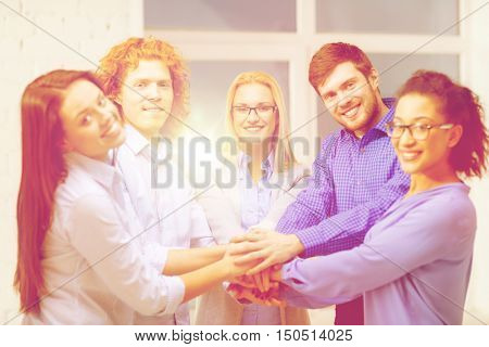 business, office, gesture and startup concept - smiling creative team with hands on top of each other sitting in office