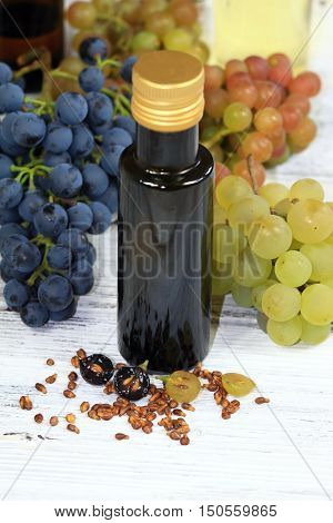 Grape seed oil and grape seeds in front fresh grapes around