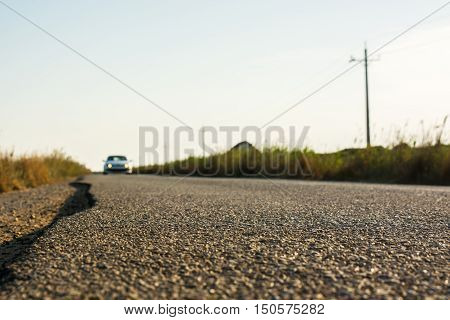 Detail of the asphalt of a country road while a car aproaches