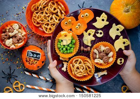 Child hands puts on the table plate with variety of treats at Halloween theme party top view