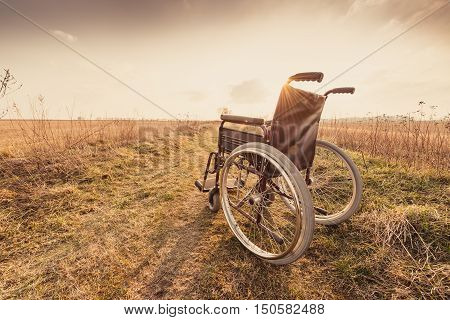 Empty wheelchair on the meadow at sunset. Miracle concept. Healed person raised and went away - retro vintage version