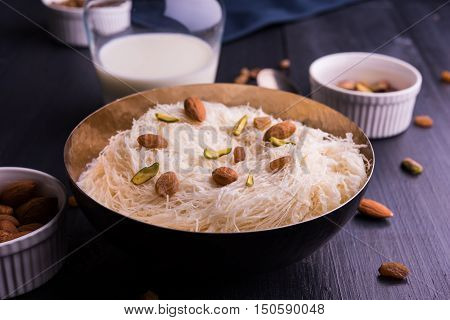 Indian sweet sutarfeni or sutar feni or firni or seviyan or laccha, shredded, flaky-rice-flour roasted in ghee, blended with melted sugar to form a cotton candy, topped with pistachio and almonds