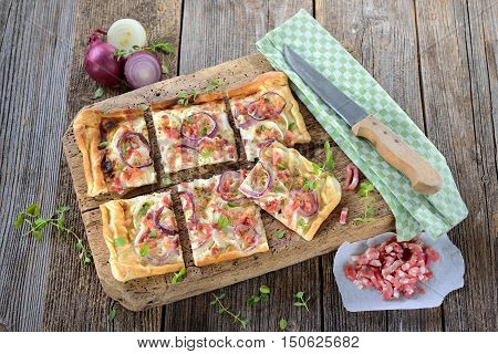 Hot baked tarte flambee from Alsace with onions, bacon and sour cream served on a shabby wooden cutting board