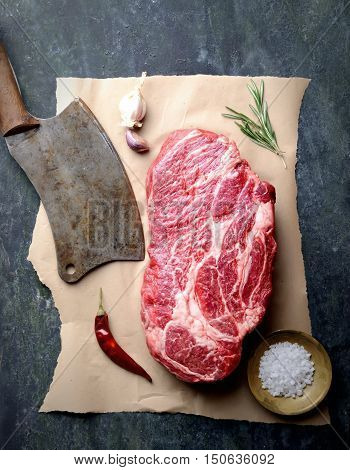 raw beef marble on paper knife for meat, rosemary, pepper and salt on a dark backgroun