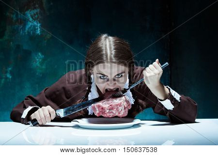 Portrait of a young girl with knife fork and and a piece of raw meat on a plate. Girl in school uniform as killer. The image in the style of Halloween and Addams family