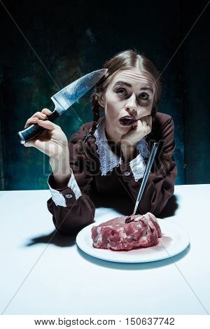 Portrait of a young girl with knife fork and and a piece of raw meat on a plate. Girl in school uniform as killer. The image in the style of Halloween and Addams family