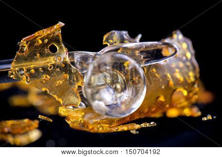 A piece of cannabis oil concentrate aka shatter with glass tools isolated against black background