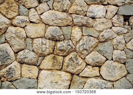 Beige stone wall facade of rocks of various sizes and forms outdoors on natural mural background