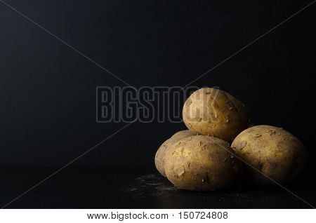 Whole, Unpeeled Potatos On Black With Soil