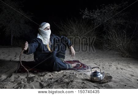 Man in traditional Tuareg outfit in a desert preparing tea