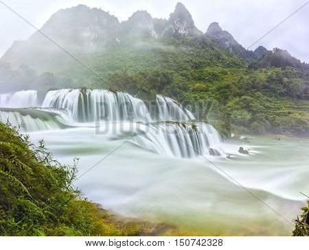 Ban Gioc Waterfall craggy limestone permissive side misty morning with grass and tones of lower cascade. It is considered most beautiful waterfalls in Southeast Asia and a national scenic Vietnam