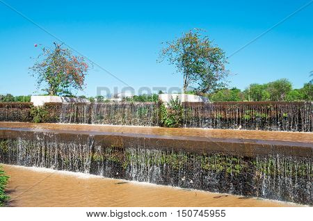 Falling cascading water of a lake in a park. Vegetation around with plants and some flowers. Beautiful sunny day with blue sky background. Natural wonders of South America.