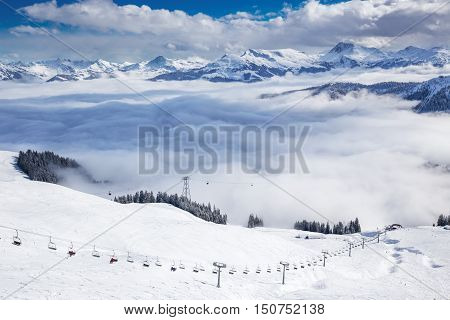 Kitzbuehel, Austria, February 17, 2016 - Skiers On Ski Lift Enjoying The View To Foggy Alps In Austr