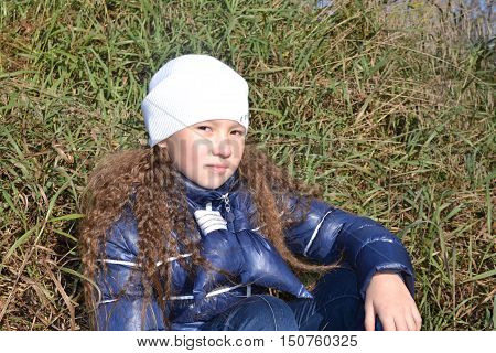 A girl with curly hair sits on a faded grass and looks ahead