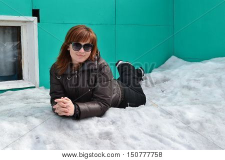 The girl in brown jacket and dark glasses lying on snow