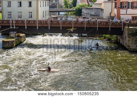 Bamberg Germany - May 22 2016: Tourists on a bridge and kayak slalom on the River Regnitz Bamberg Bavaria Germany Europe. The historic city center is a listed UNESCO world heritage site.