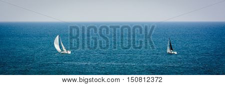 A couple of yachts sailing by sea on a foggy day.