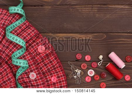 Red fabric , thread, measuring tape and buttons on the wooden table. The view from the top. Sewing accessories.