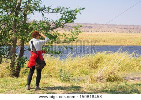 Tourist Watching Wildlife By Binocular On Chobe River, Namibia Botswana Border, Africa. Chobe Nation