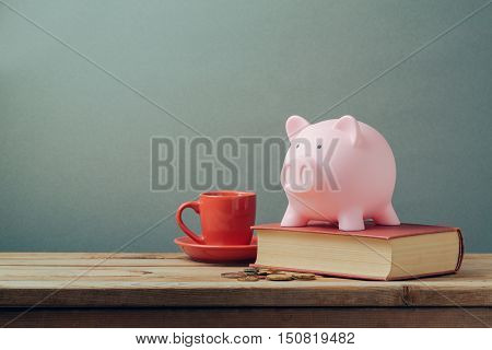 Piggy bank on wooden table with coffee cup and book. Saving money budget planning concept.