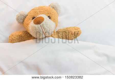 Brown Teddy Bear lying on a bed with white linen and pillowcases.