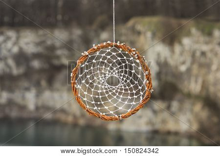 Handmade dream catcher on background of rocks and lake. Tribal elements feathers