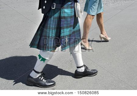 A man dresed up a Scottish kilt‎ and a woman wearing a dress walks down the street.