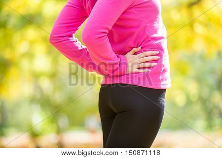 Warming up outdoors in the autumn, hands on the hips, back ache position. Concept photo, closeup