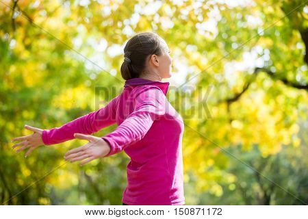 Portrait of an attractive smiling woman outdoors in a sportswear, her hands outstreched. Indian summer. Concept photo, side view