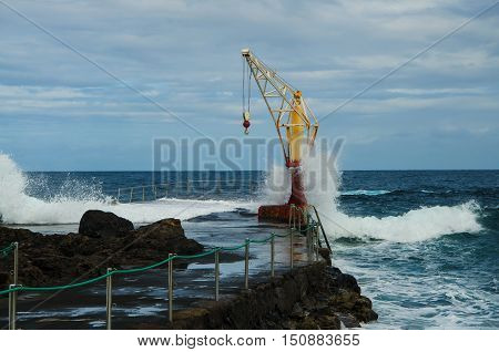 Storm ocean waves hitting old boat crane