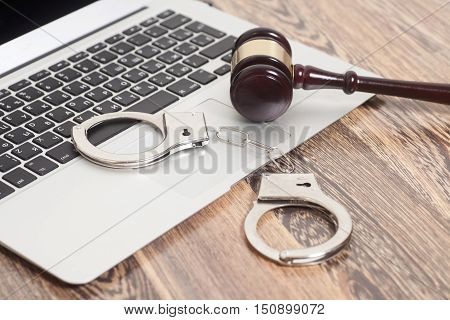 Handcuffs and gavel on laptop on wooden background