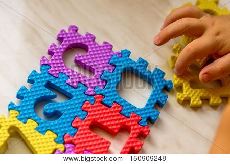 Colorful foam puzzle letters and numbers in kid's hands on a light table. Baby puts puzzle of letters and numbers. Close-up