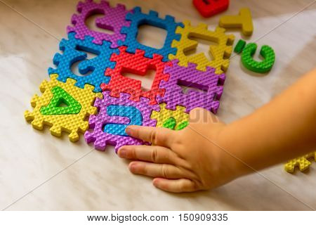 Colorful foam puzzle letters and numbers in kid's hands on a light table. Baby puts puzzle of letters and numbers. Close-up