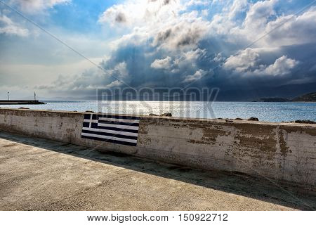 Picture of Greek flag on wall of promenade with stormy sky in Sitia town, Crete island, Greece