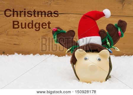 Having a Christmas Budget Piggy bank with Christmas hat on snow with a weathered wood background with text Christmas Budget