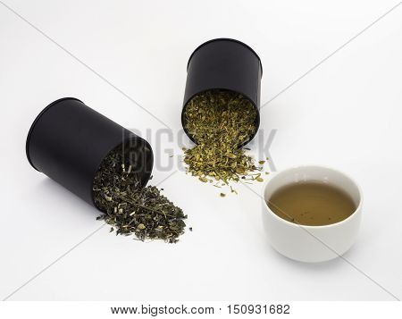Two canisters of herbs spilling onto background with a cup of tea