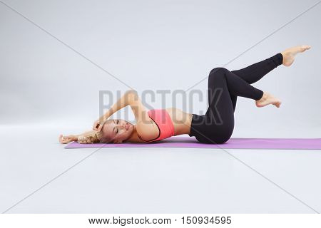 Young blonde slim girl is stretching in the studio on the white background