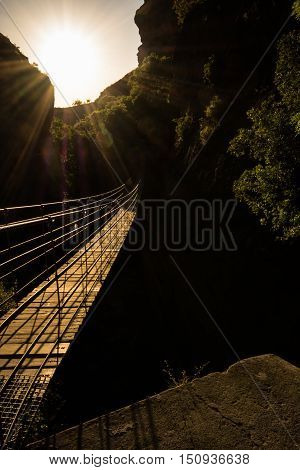 Hanging bridge over a deep and dark canyon against the sun