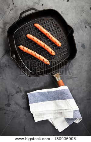 Top view of three hot Vienna sausages on the grill pan on a gray background with a kitchen towel nearby. Ingredients for making homemade hot dogs. Perfect lunch with easy dish. Fast food snack